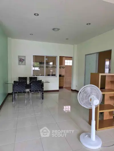 Spacious dining area with modern furniture and fan, leading to a bright kitchen.