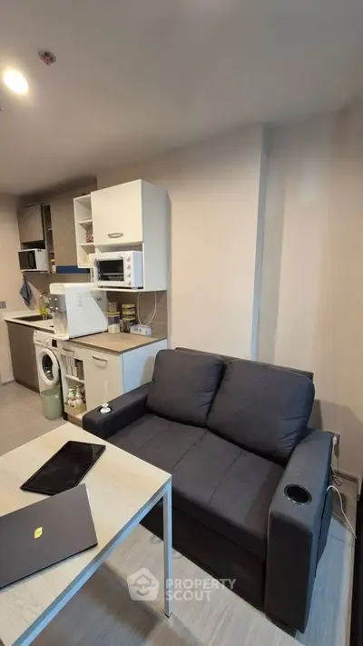 Modern compact living room with integrated kitchen, featuring sleek appliances and cozy seating area.