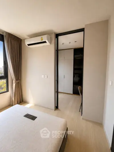Modern bedroom with air conditioning and natural light, featuring a view of the cityscape.