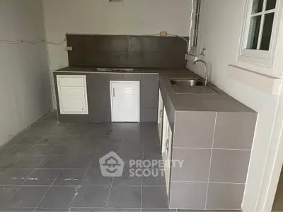 Spacious kitchen with tiled countertops and sink, ideal for culinary enthusiasts.