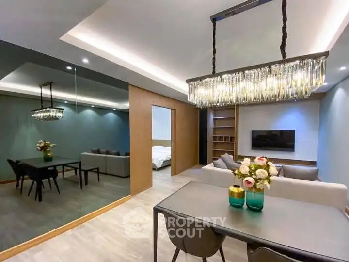 Modern open-plan living and dining area with elegant chandelier and mirrored wall.