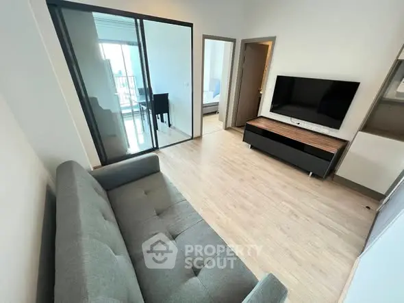 Modern living room with sleek furniture and large glass doors leading to a bright balcony.