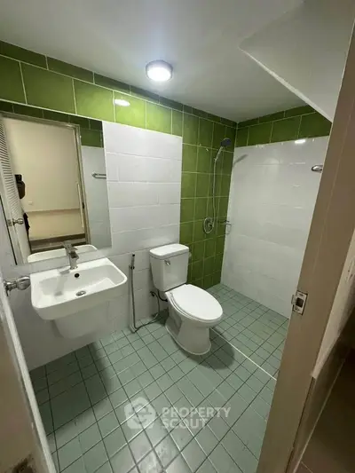 Modern bathroom with green and white tiles, featuring a shower and toilet.