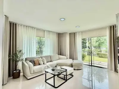 Spacious living room with large windows and garden view, modern white sofa and elegant decor.