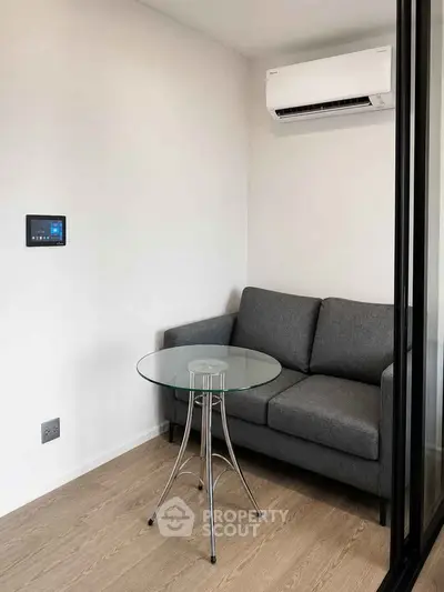 Modern small living room with gray sofa, glass table, and wall-mounted air conditioner.