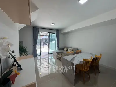Modern living room with marble dining table and cozy seating area, featuring large windows for natural light.