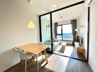 Modern living room with glass partition and dining area, featuring natural light and stylish furniture.