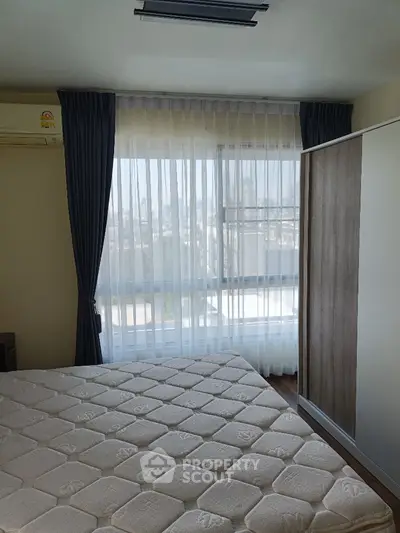 Bright bedroom with large window and city view, featuring modern wardrobe and air conditioning.