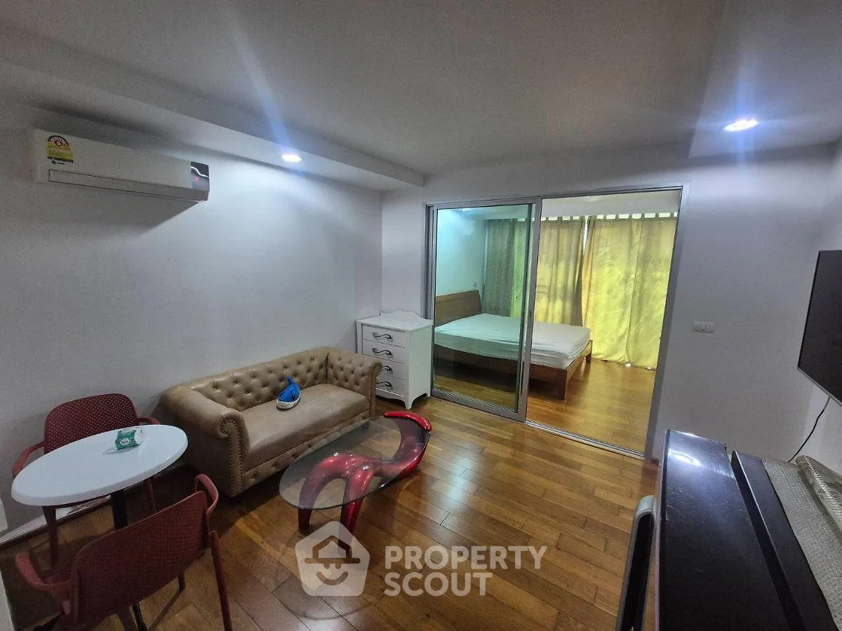 Modern living room with wooden flooring, cozy sofa, and sliding glass doors leading to a bedroom.