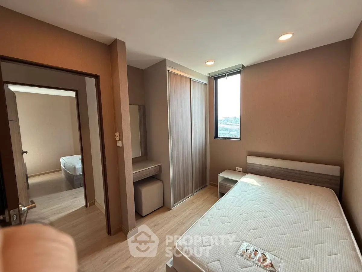 Modern bedroom with natural light, featuring a comfortable bed and sleek wooden flooring.