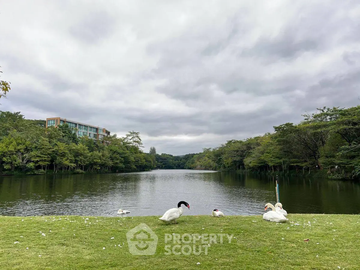 Serene lakeside view with lush greenery and modern building, perfect for tranquil living.