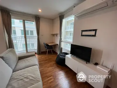 Spacious and well-lit living room with hardwood flooring, modern furniture, and a cozy balcony, perfect for urban living.