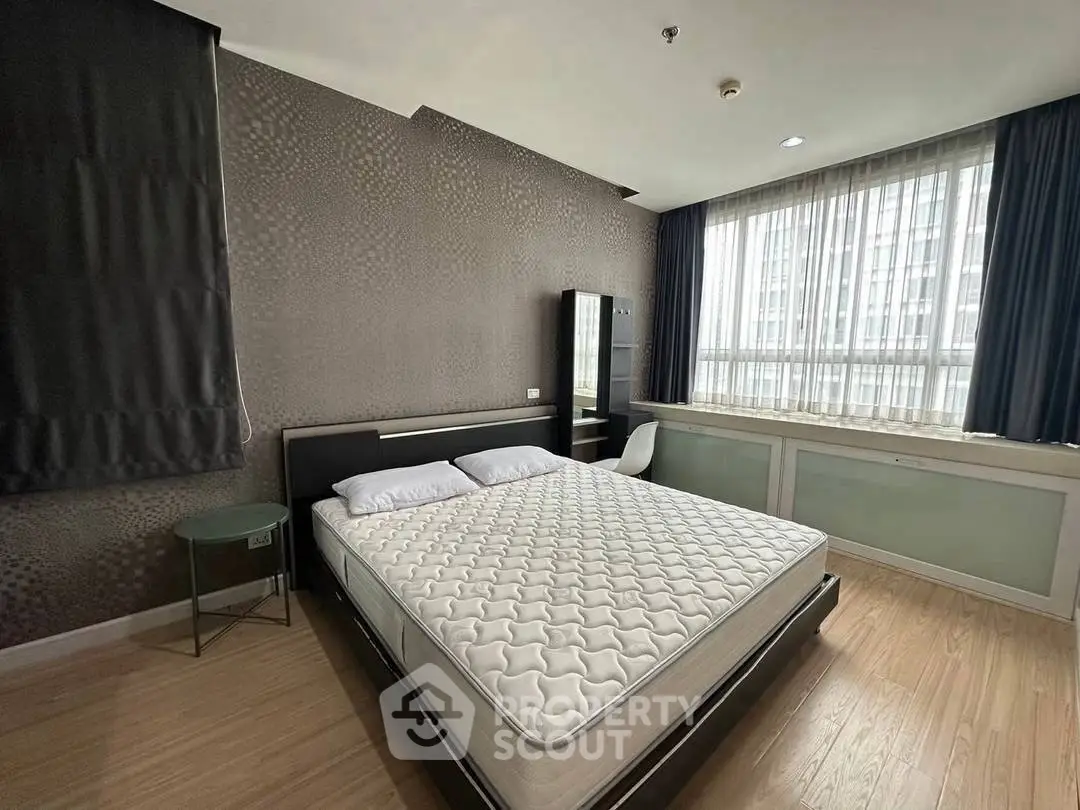 Spacious modern bedroom with large window and stylish decor in urban apartment.