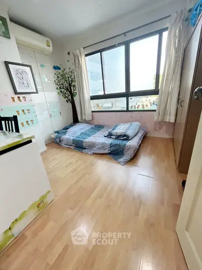 Cozy bedroom with wooden flooring and large window, perfect for natural light lovers.