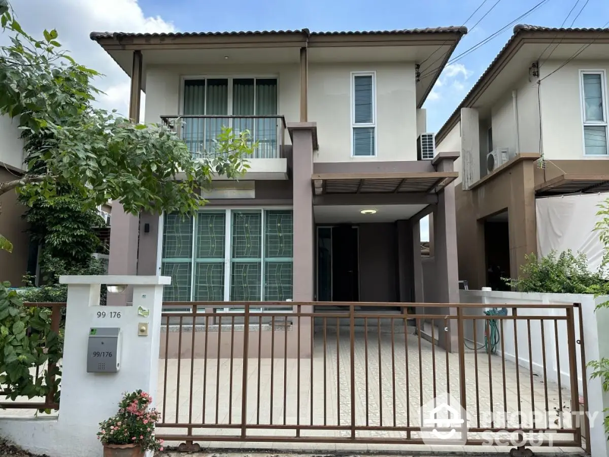 Modern two-story house with balcony and gated entrance in a suburban neighborhood.