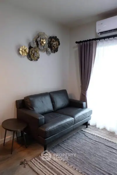 Cozy living room with modern sofa, stylish wall decor, and natural light from large window.