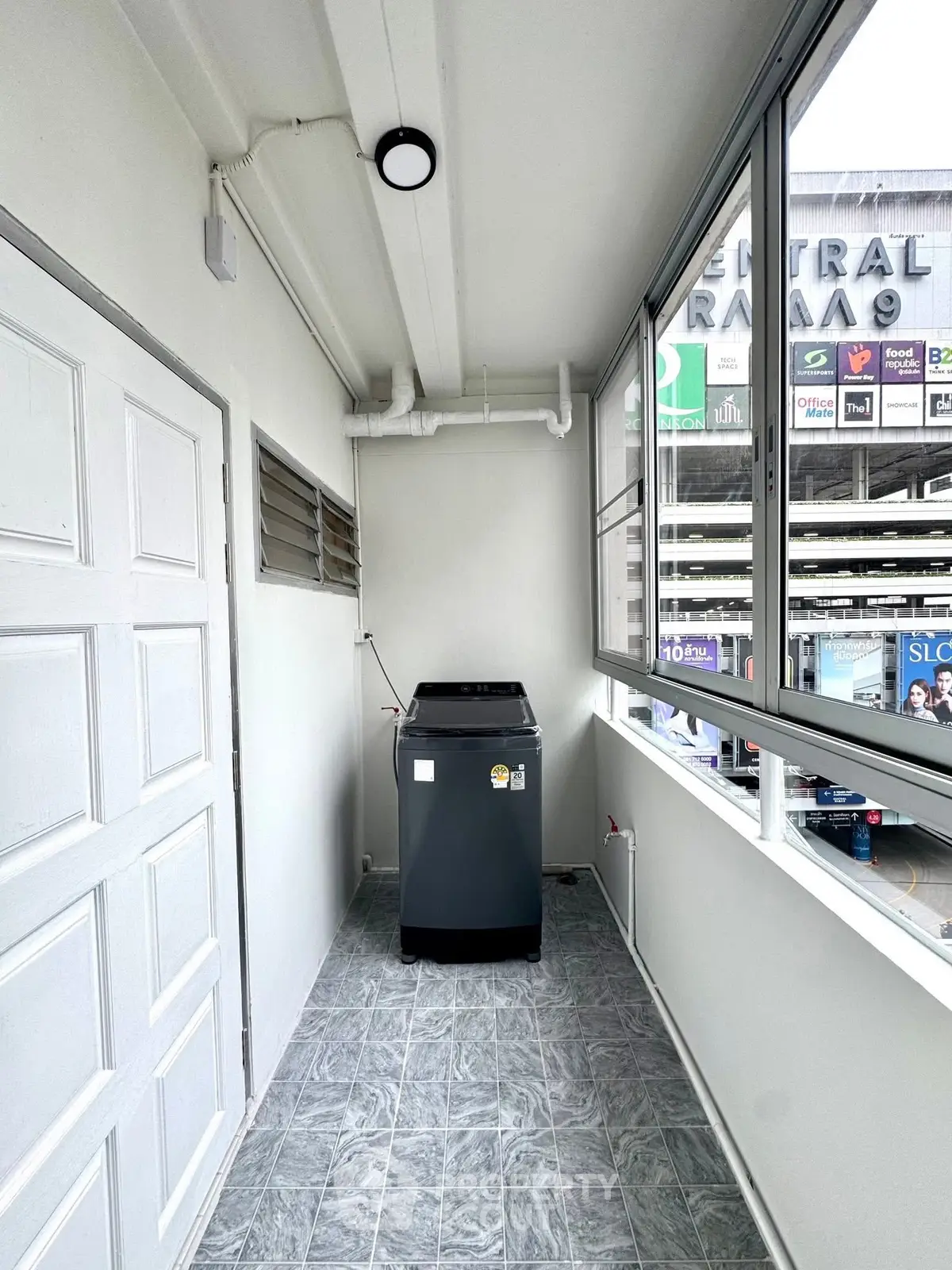 Compact laundry area with washing machine and large windows in modern apartment.