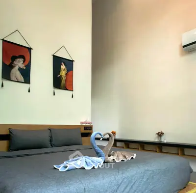 Cozy bedroom with elegant decor and air conditioning, featuring artistic wall hangings and swan towel arrangement.