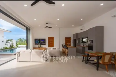 Luxurious open-plan living room with pool view, modern kitchen, and elegant furnishings in a contemporary home.