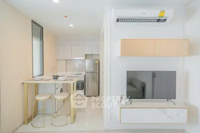 Modern kitchen and living area with sleek design and neutral tones, featuring a compact dining space and wall-mounted TV.