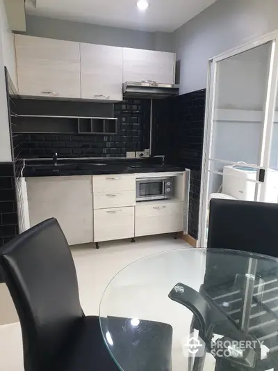 Modern kitchen with sleek black and white design, featuring glass dining table and built-in microwave.