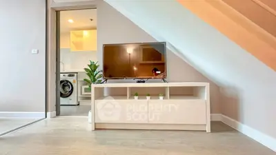 Modern living room with TV under staircase and view into kitchen with washing machine.