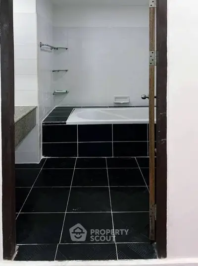 Modern bathroom with black tile flooring and built-in bathtub, featuring sleek design and minimalist shelves.