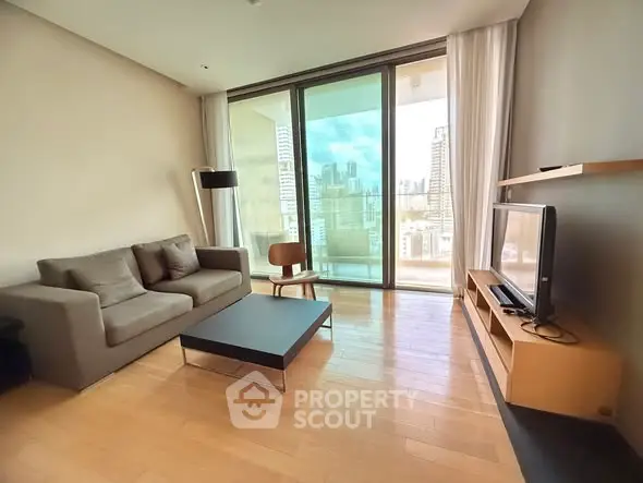 Modern living room with city view, sleek furniture, and large glass doors leading to balcony.