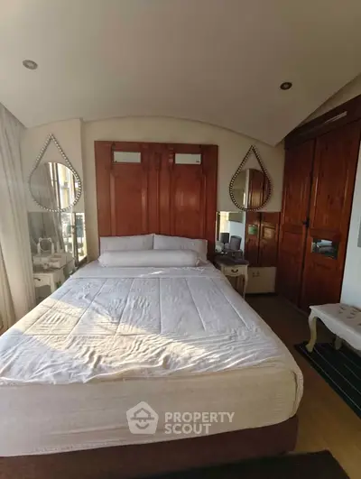 Elegant bedroom with wooden accents and stylish mirrors, featuring a cozy bed and ample natural light.