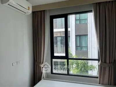 Modern bedroom with large window and air conditioning, offering a view of neighboring building.