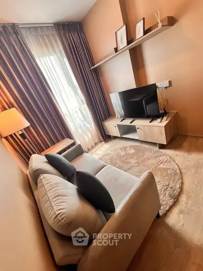 Cozy living room with modern decor and natural light, featuring a plush sofa and flat-screen TV.