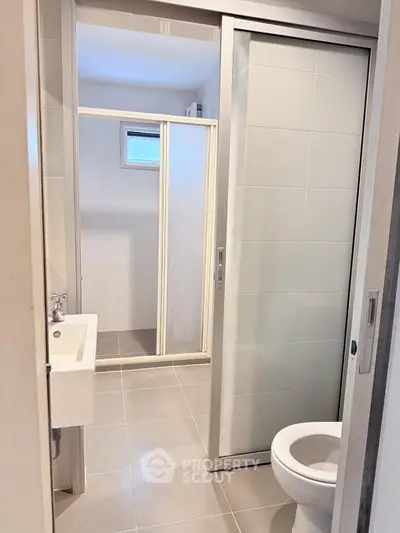 Modern bathroom with sliding door and compact design, featuring a shower and sleek fixtures.
