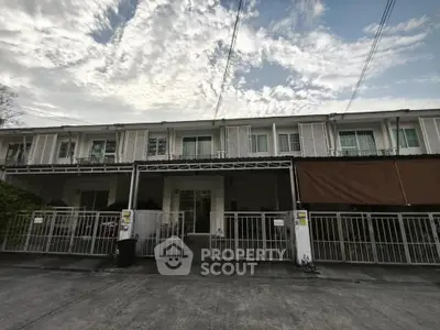 Charming townhouse with gated entrance and modern facade under a picturesque sky.