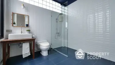 Modern bathroom with sleek glass shower enclosure, white subway tiles, and a classic wooden vanity, offering a blend of contemporary design and traditional charm.