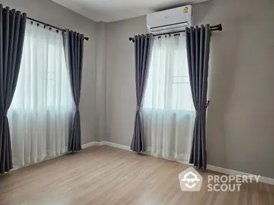 Spacious and well-lit living room with elegant dark curtains and modern air conditioning unit, featuring sleek wooden flooring.