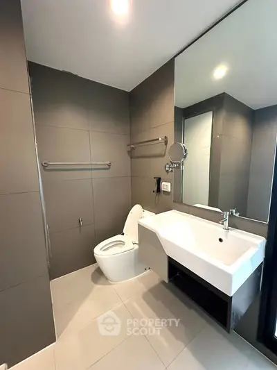 Modern bathroom with sleek design and large mirror, featuring a stylish sink and toilet.
