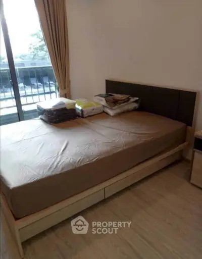 Cozy bedroom with balcony access and natural light, featuring a neatly made bed and wooden flooring.