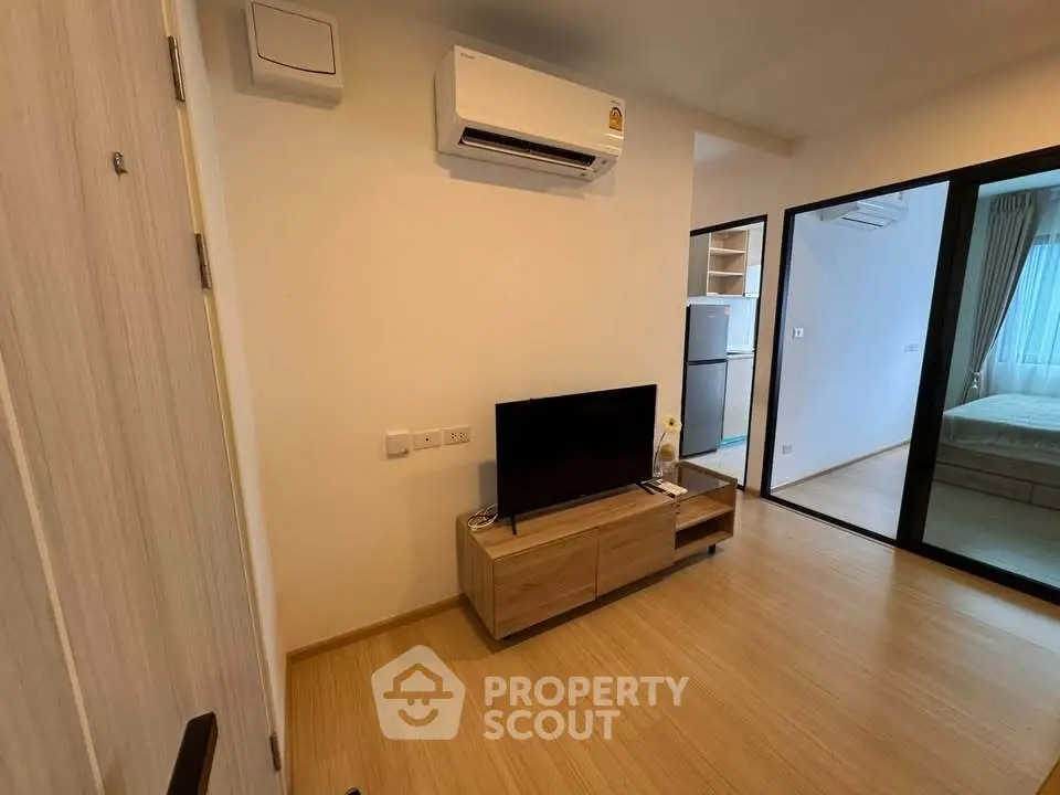 Modern apartment interior with air conditioning and wooden flooring, featuring a cozy living area and bedroom view.