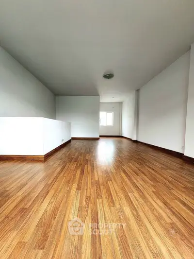 Spacious empty room with wooden flooring and white walls, ideal for customization.
