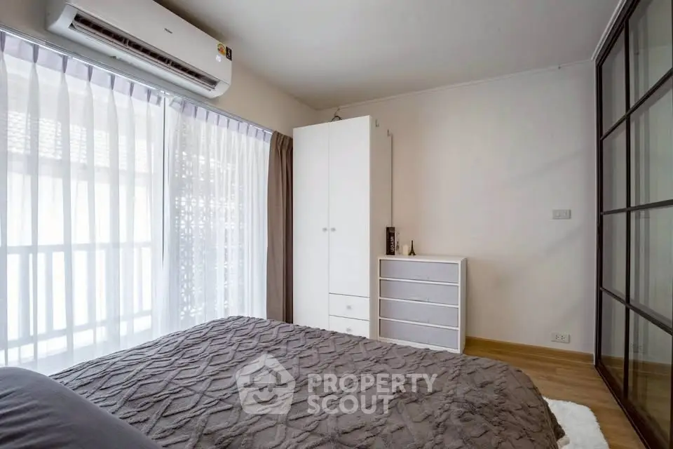 Cozy bedroom with large window and modern air conditioning unit, featuring stylish decor and ample natural light.