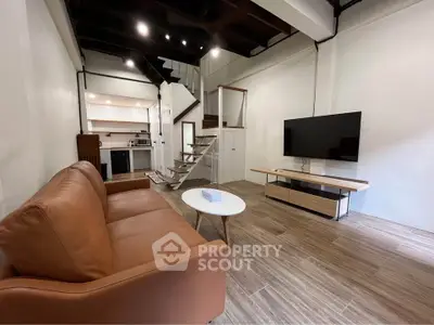 Modern living room with leather sofa, flat-screen TV, and stylish staircase in open-concept loft.