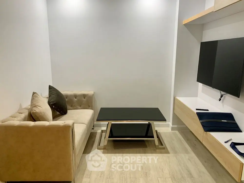 Modern minimalist living room with beige sofa, sleek black coffee table, and wall-mounted TV.