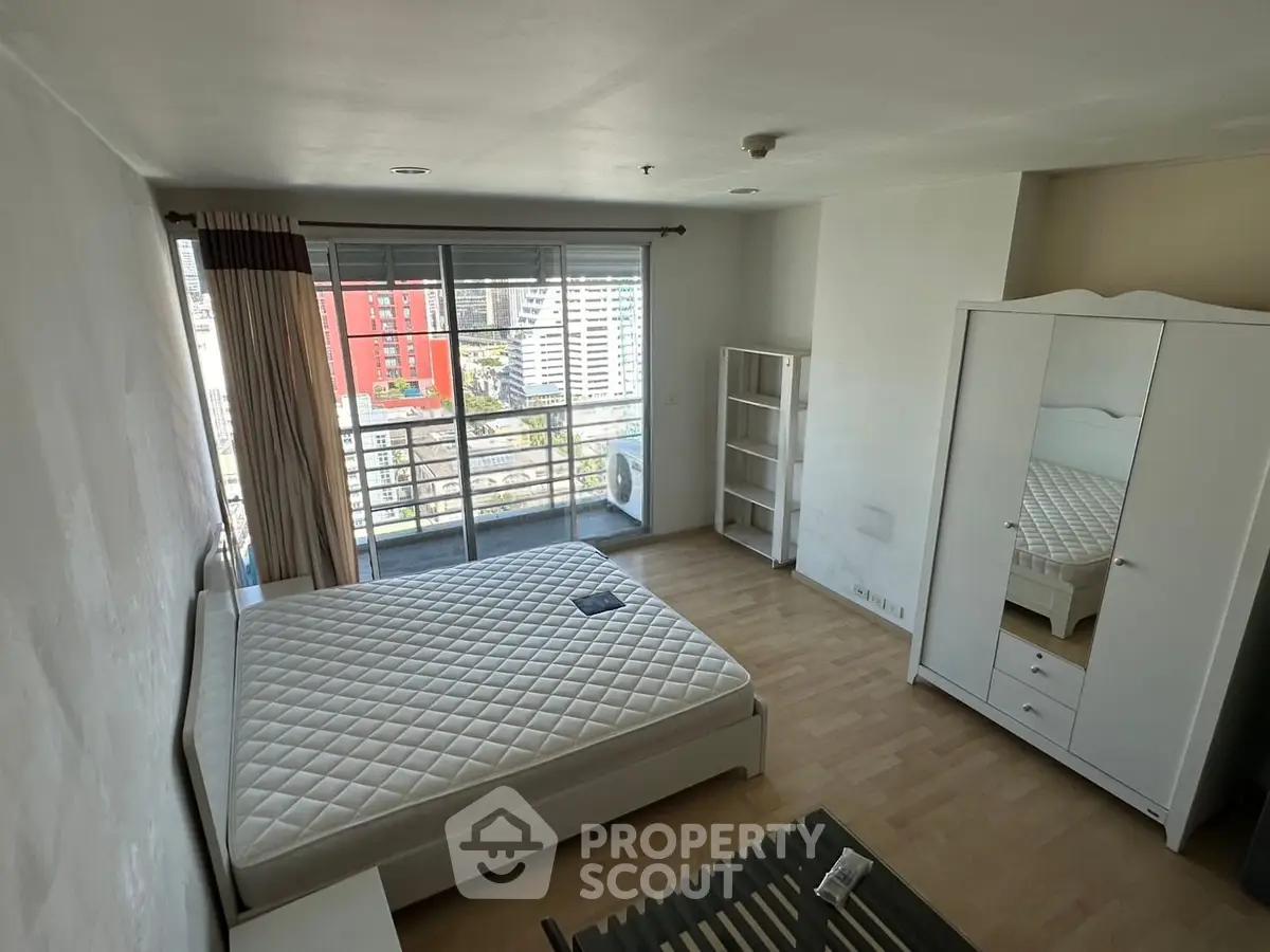 Spacious bedroom with large window and city view, featuring modern furniture and ample natural light.