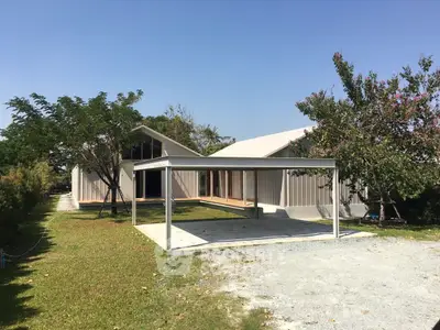 Modern single-story house with spacious garden and carport under clear blue sky.