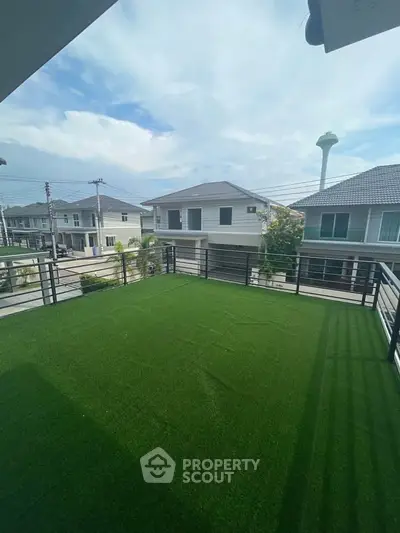 Spacious balcony with artificial grass and scenic neighborhood view.