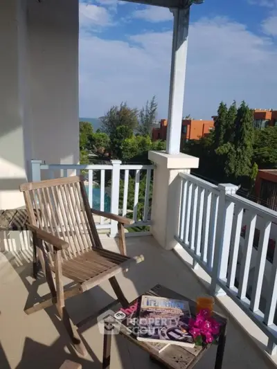 Charming balcony with wooden chair and table overlooking lush greenery and distant view.