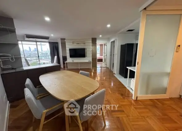 Spacious open-plan living and dining area with city view, featuring modern furniture and wooden flooring.
