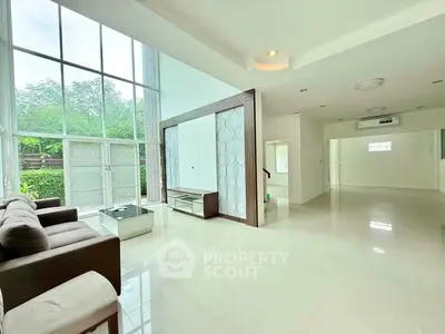 Spacious modern living room with high ceilings and large windows offering natural light and garden view.