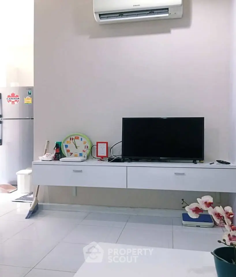 Modern living room with sleek TV unit and air conditioning, adjacent to a kitchen area with a fridge.
