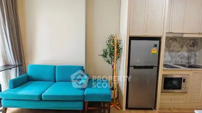 Modern living room with vibrant blue sofa and sleek kitchen appliances in a cozy apartment.